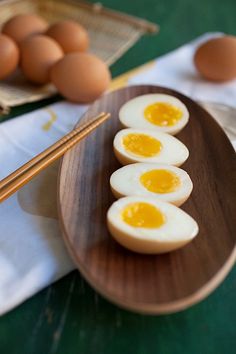 three hard boiled eggs on a wooden plate with chopsticks next to the plates