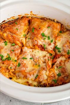 a white crock pot filled with lasagna casserole covered in cheese and parsley