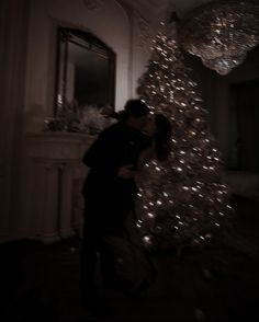 a man and woman are kissing in front of a christmas tree with lights on it