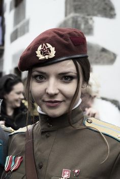 a woman in uniform is smiling for the camera while people are walking by behind her