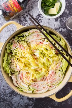 a bowl filled with salad and chopsticks on top of a table next to other food