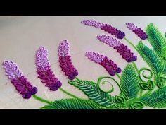 some purple flowers and green leaves on a white table cloth with embroidery work in the middle