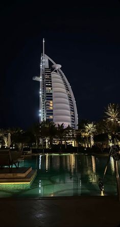 the burj building is lit up at night in front of a swimming pool