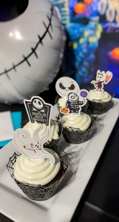 three cupcakes with white frosting on a plate next to a halloween decoration