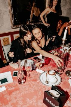 two women sitting at a dinner table with wine glasses and candles in front of them