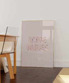 a pink poster with the words love rules in gold foil on it next to a chair