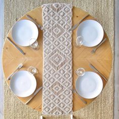 the table is set with white plates and silverware on it, along with a crocheted placemat