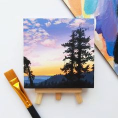 two paintings on easels with paintbrushes next to them