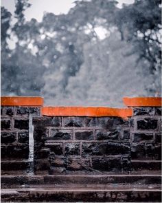 an orange brick wall with trees in the background and snow falling down on it's sides