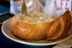 a person is cutting into a bowl of soup on a plate with two pieces of bread