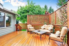 a wooden deck with chairs and table next to a fenced in area that has trees on it