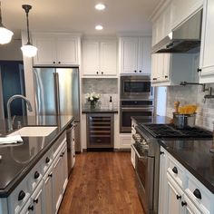 a kitchen with white cabinets and black counter tops, stainless steel appliances and wooden floors