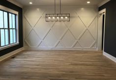 an empty room with wood flooring and black accent walls, along with a chandelier hanging from the ceiling