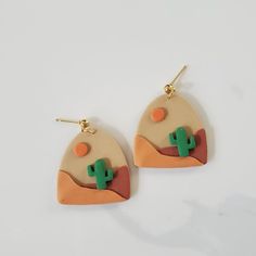 a pair of earrings with an orange and green cactus on it, sitting on top of a white surface