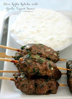 several skewered meatballs are sitting on a plate next to a bowl of yogurt sauce