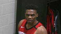 a man in a red jersey standing next to a wall with baseball bats on it