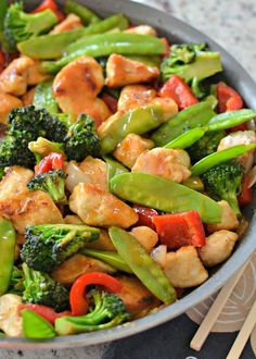 stir fry with chicken, broccoli and peppers in a pan next to chopsticks