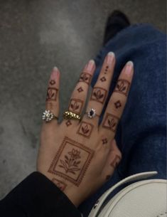 a woman's hand with henna tattoos and rings on her left hand, next to a white shoe