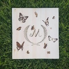 a wooden sign with butterflies and the letter m on it sitting in some green grass