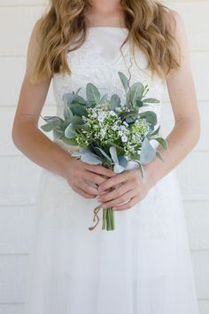 a woman wearing a white dress holding a bouquet of flowers and greenery in her hands