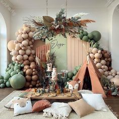 a table topped with lots of balloons next to a teepee tent and other decorations