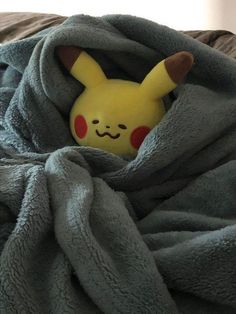 a stuffed pikachu pokes out from under a blanket