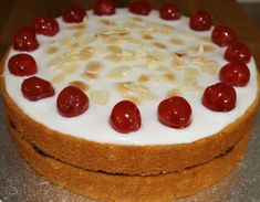 a cake with white frosting and red cherries on top is sitting on a table