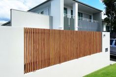 a white house with wooden slats on the fence and cars parked in the driveway