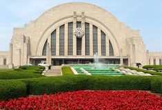 a large building with a fountain in front of it and red flowers around the perimeter