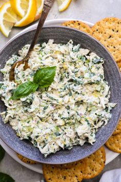 a bowl filled with spinach dip surrounded by crackers and lemon wedges on the side