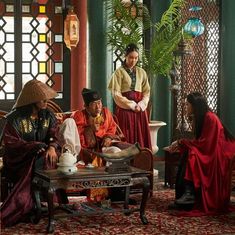 several people dressed in traditional chinese clothing sit around a table and talk to each other