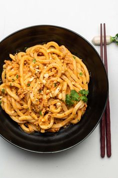 a black bowl filled with noodles and meat next to chopsticks on a white surface