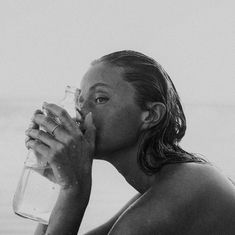 black and white photograph of a woman drinking from a water glass in front of the ocean