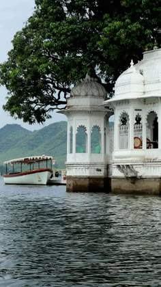 a white gazebo sitting on the side of a lake next to a boat in the water