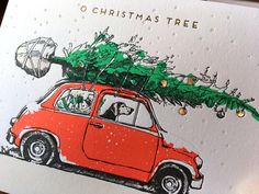 a red car with a christmas tree on the roof is parked in front of a card