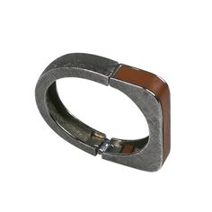 Castlecliff Modernist leather trimmed bracelet. Hinged bangle with one squared end and one rounded. Crosshatched silvered metal with light brown leather trim. .5" wide, 2.25" x 1.75" interior measure. 1960's USA. Excellent condition.