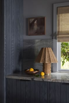 a lamp sitting on top of a counter next to a bowl of lemons and a painting