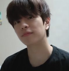 a young man with dark hair and black shirt looking at the camera while standing in front of a white wall