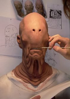 a woman is painting the head of an old man's head with pencils