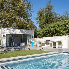 a backyard with a swimming pool surrounded by trees and grass, next to a white house