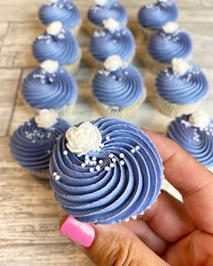 a hand is holding a blue cupcake with white frosting on it and there are more cupcakes in the background