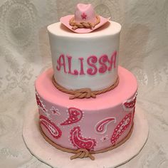 a three tiered cake decorated with pink and white frosting, cowboy hat on top