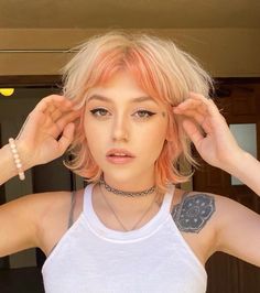 a woman with pink hair wearing a white tank top and silver bracelets holding her hands up to her head