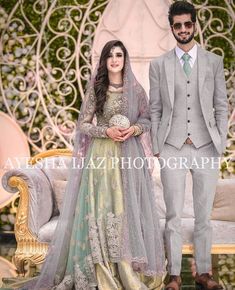 a man and woman standing next to each other in front of a white couch wearing wedding outfits