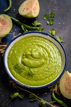 a bowl filled with green sauce next to sliced avocados