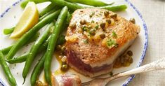 a white plate topped with meat and green beans next to lemon wedges on top of a table