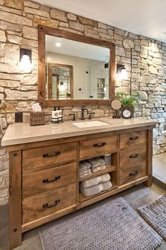 a bathroom with stone walls and wooden cabinets, mirror above the sink, and rugs on the floor