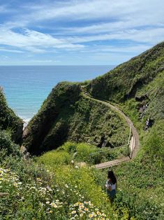 a woman is walking down a path to the beach with flowers in front of her