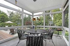 a table and chairs on a porch with sunflowers in the vase next to it