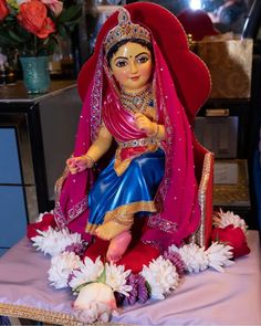 a statue of a woman sitting on top of a table with flowers in front of her